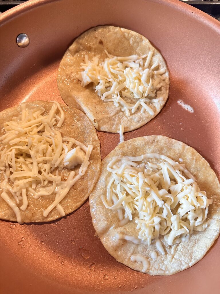 Shredded cheese on three small tortillas cooking in a pan