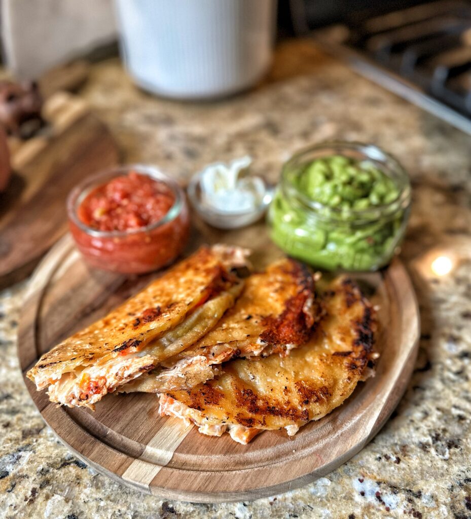 Crispy chicken tacos in front of salsa, sour cream, and guacamole 