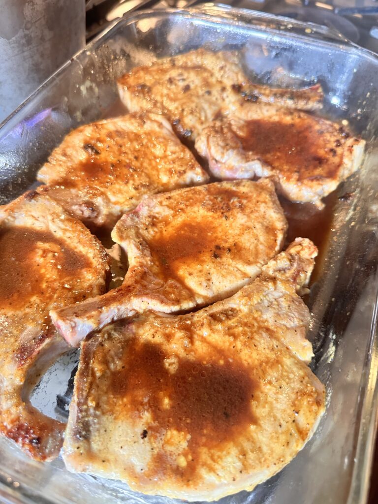 Pork chops with sauce in a baking dish.