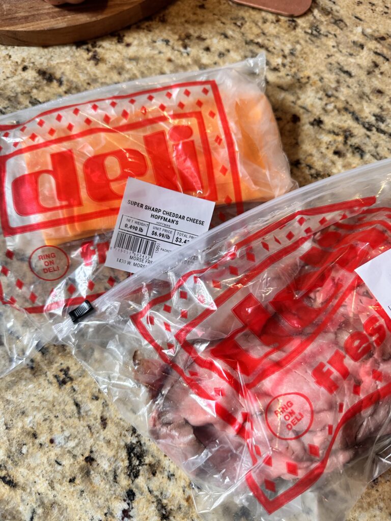 A deli bag of sliced cheddar cheese and a deli bag of sliced roast beef.