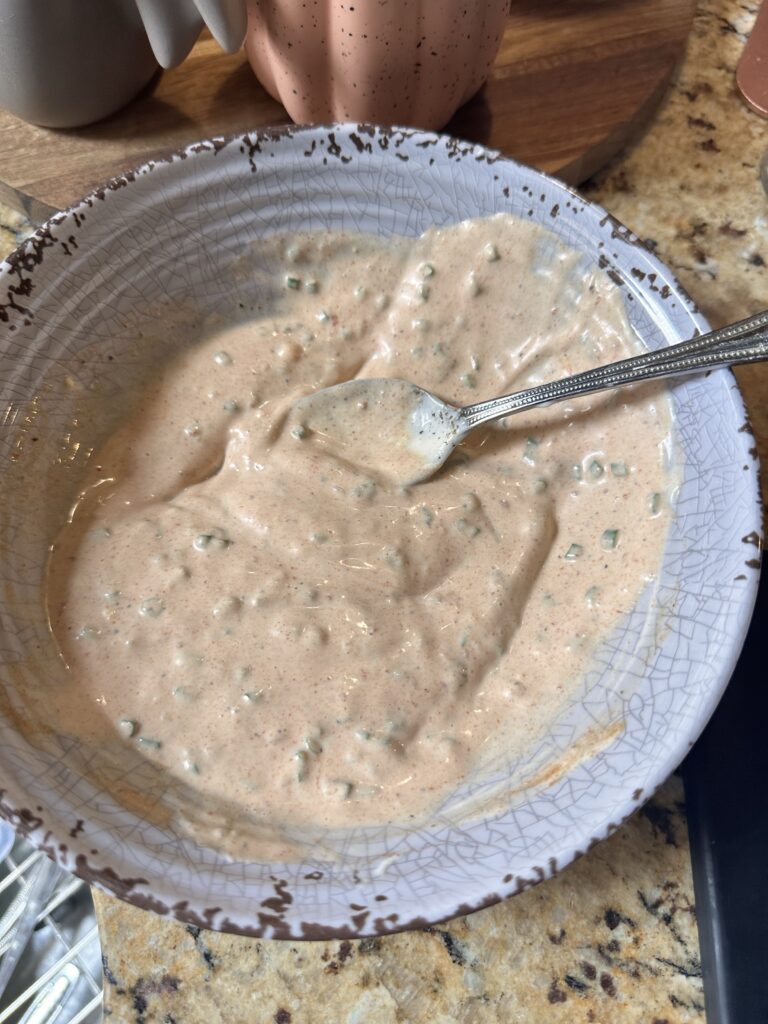 The sandwich sauce in a bowl with a spoon after being mixed together.