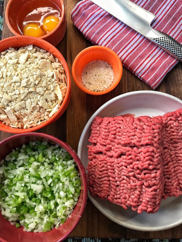 The ingredients for the meatloaf, including seasonings, ground beef, egg yolks, crushed crackers, and minced green pepper and onions
