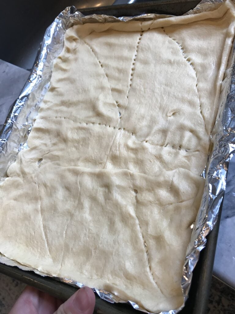 Pillsbury crescent roll dough spread out on a foil lined baking sheet.