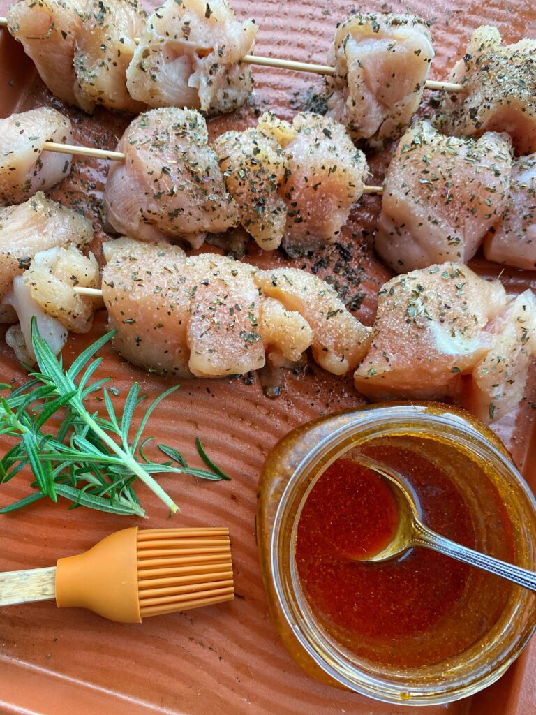 Raw, seasoned chicken skewers next to a red marinade