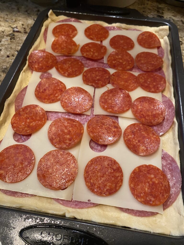 Deli meats and cheeses layered over uncooked pastry dough