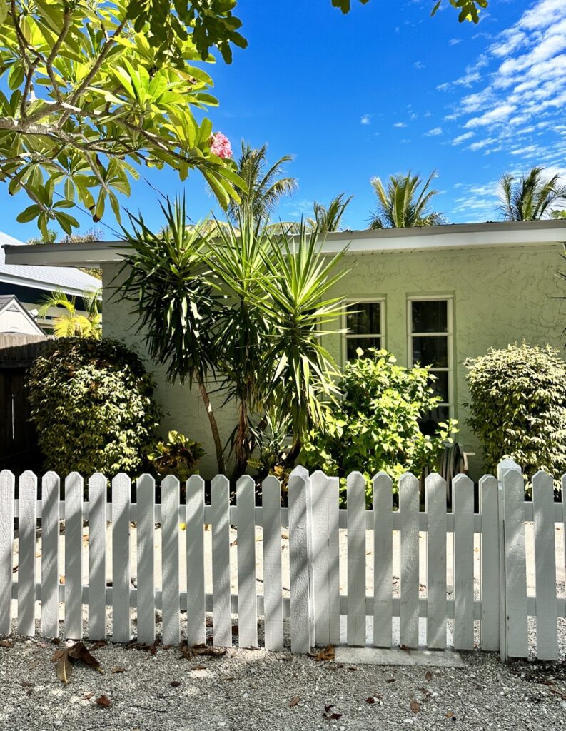 A house with trees in the yard behind a white fence.