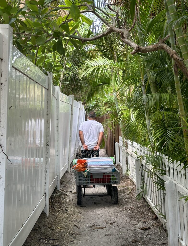 A man pulling a cart with towels behind him as he walks between two fences.