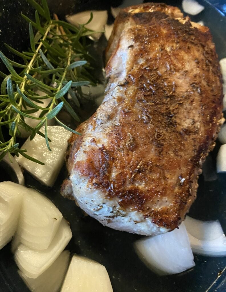 Pork cooking in a pan with onions and rosemary.