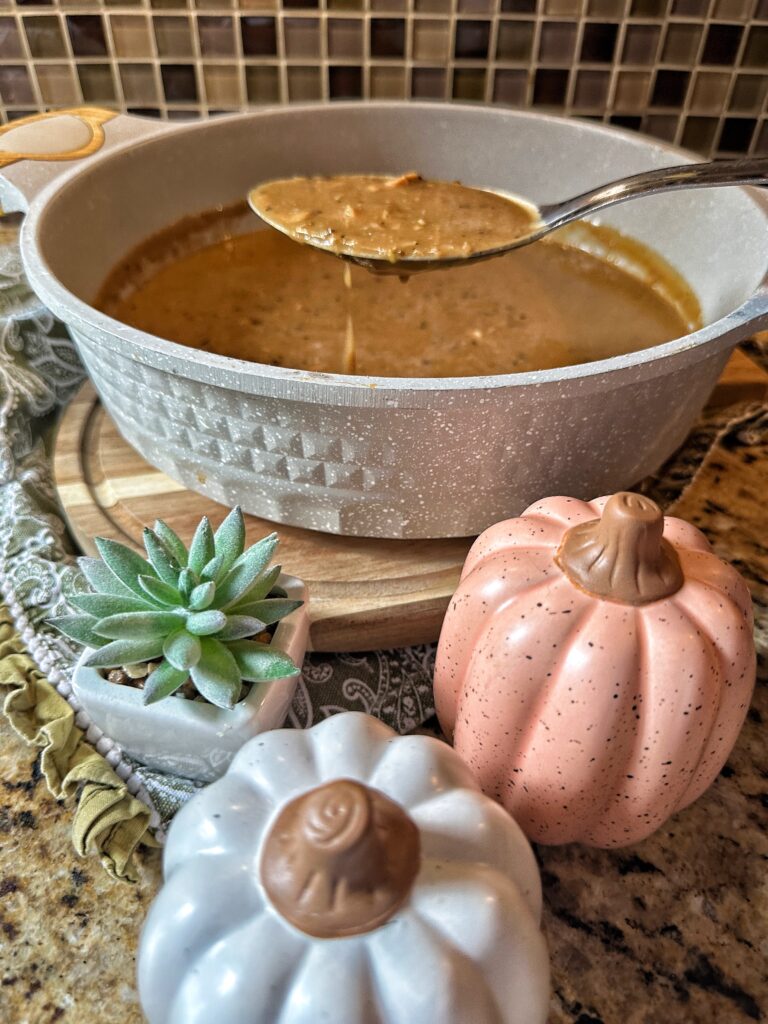A spoon of dripping gravy above ceramic pumpkins