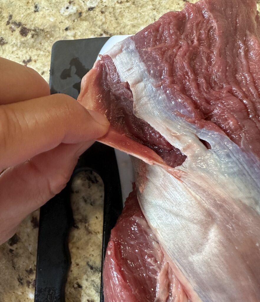 Tough, white tissue being removed from a raw beef tenderloin by hand