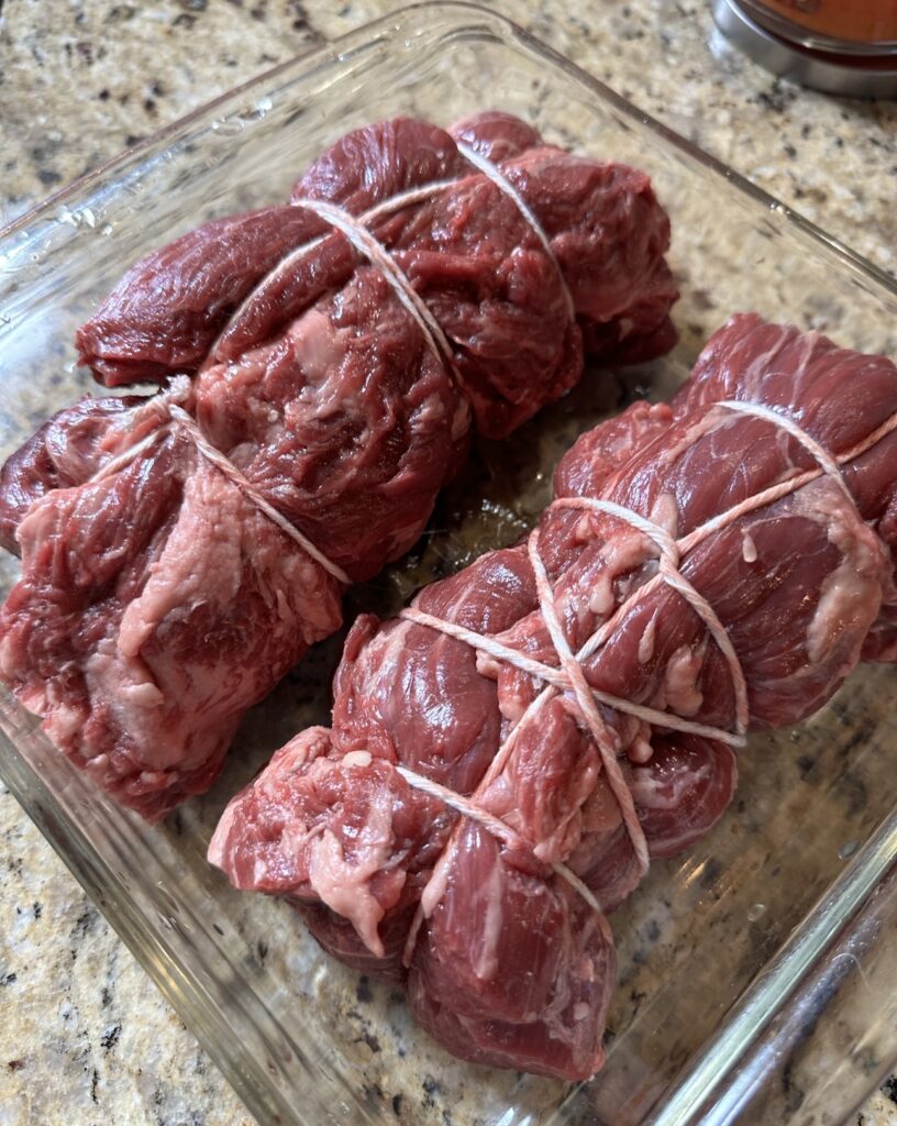 Raw beef tenderloin tied up in a glass dish