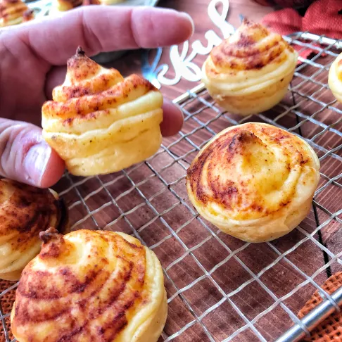 A finished potato puff being held up above other puffs