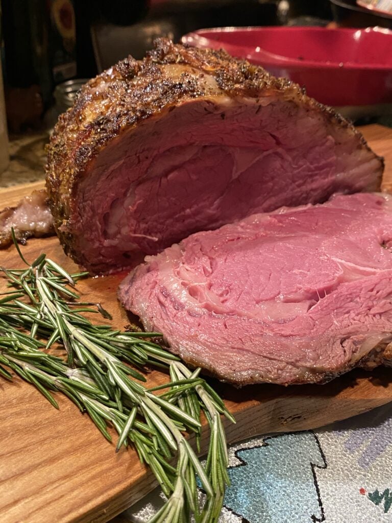 Sliced rare rib roast on a cutting board next to rosemary
