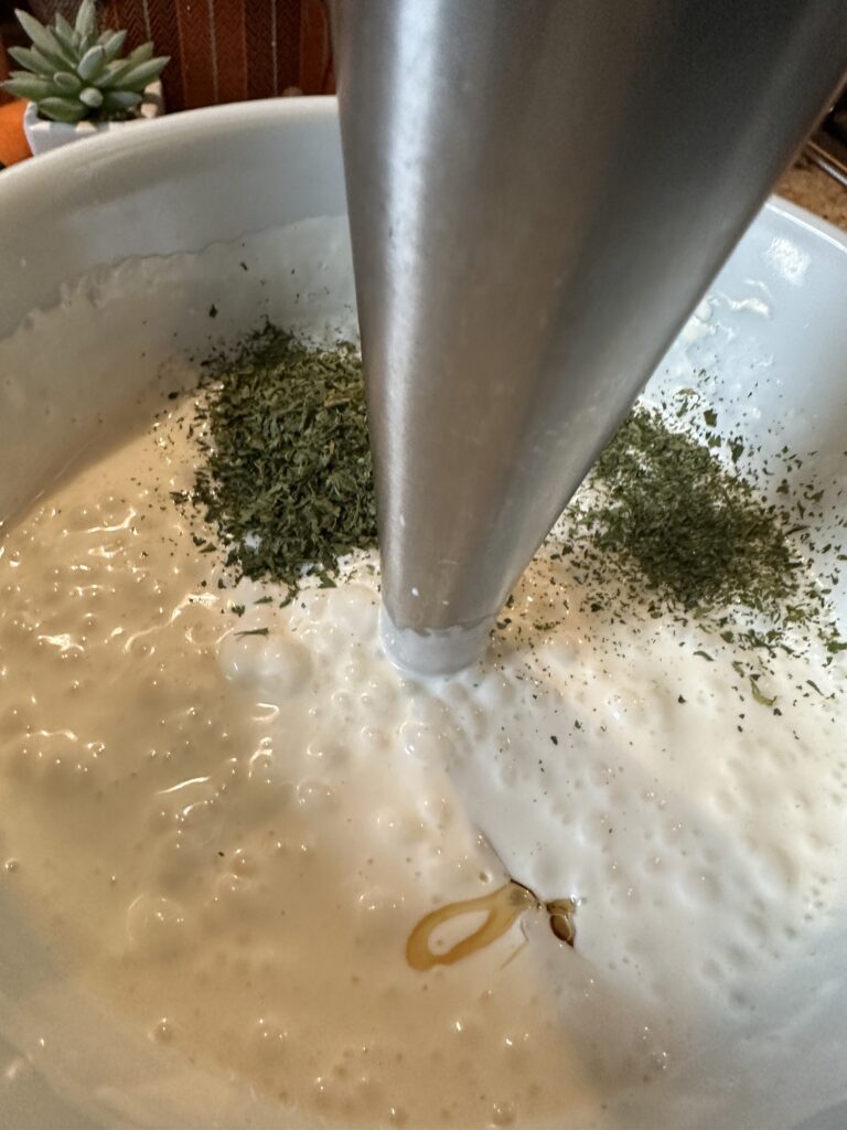 An immersion blender in a mixing bowl of dressing ingredients