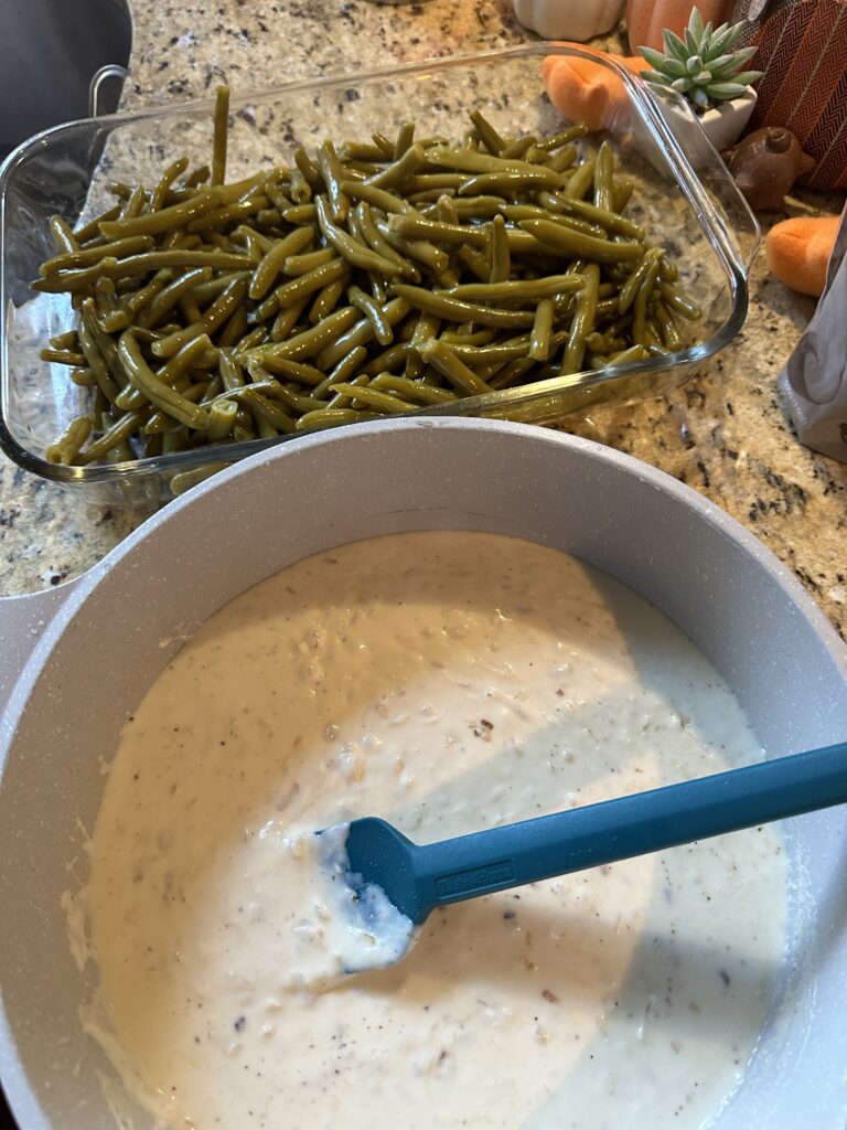 Green beans in a glass baking dish behind a bowl of white sauce