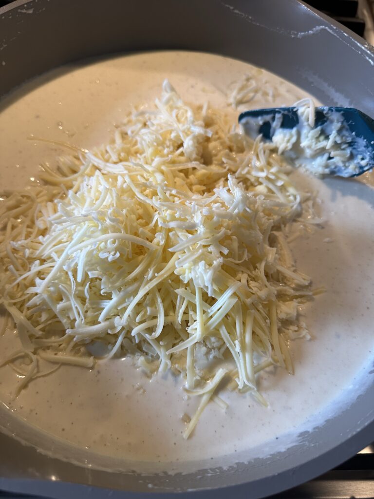 Shredded cheese being added to the sauce mixture