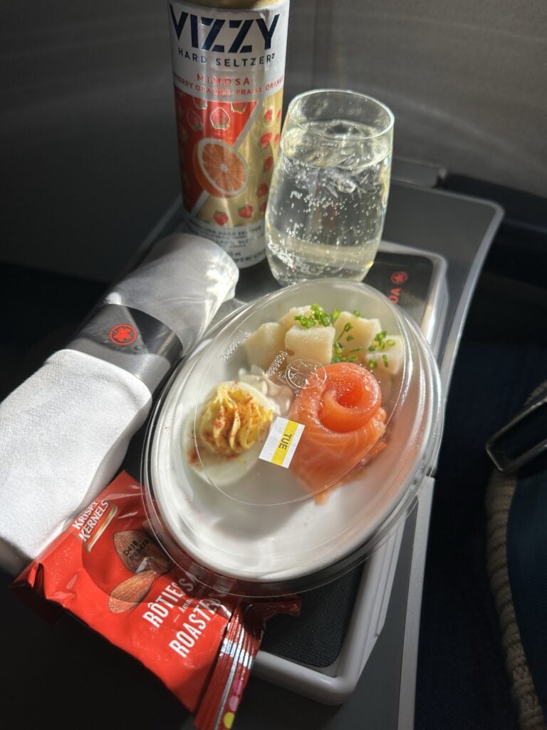 Seltzer, a deviled egg, salmon, potatoes, and a package of almonds on an airplane tray