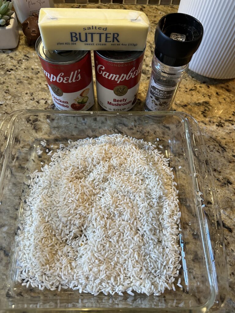 Uncooked rice in a glass baking dish next to two types of Campbell's Soup and peppercorns