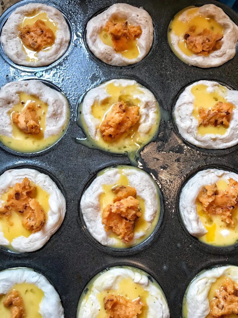 Cheese on top of egg yolk on top of raw biscuit dough in a muffin tin