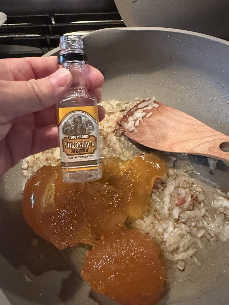 A small, empty bottle of honey whiskey held over the cooking mixture
