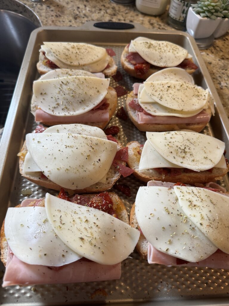 Cheese, meats, and seasoning on bread on a baking sheet