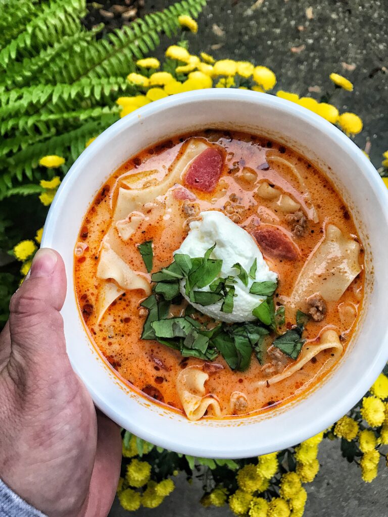 A bowl of lasagna soup with cheese and basil topping