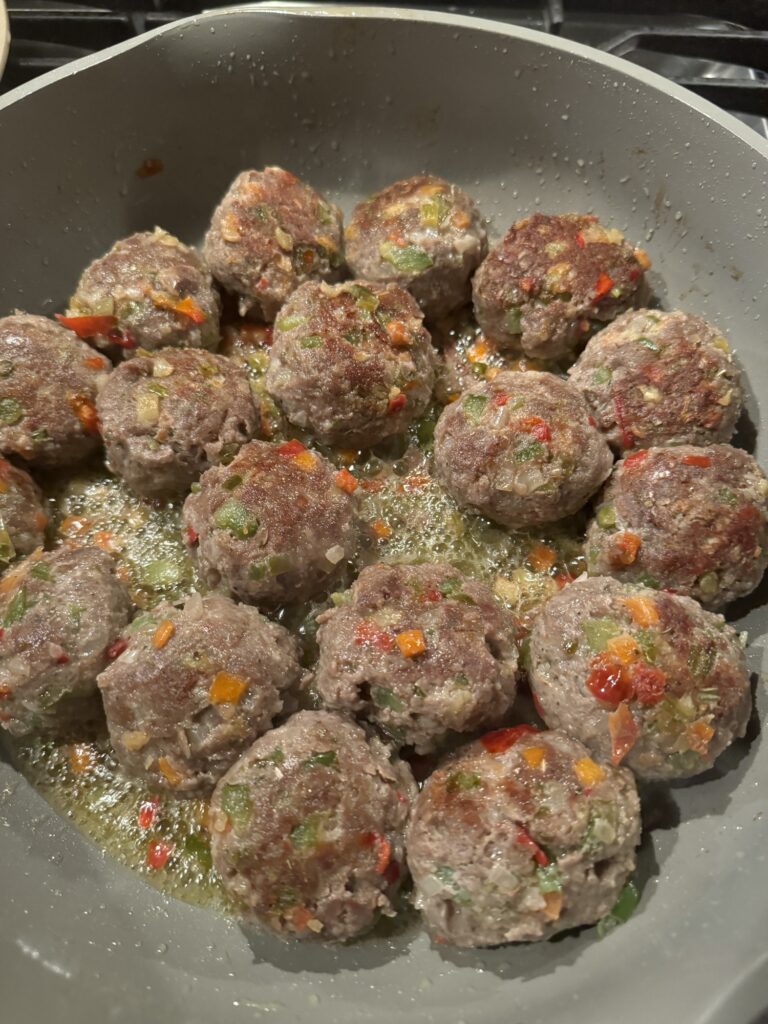 The raw Italian meatballs cooking in a skillet