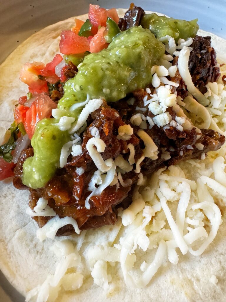The tangy shredded meat served as a taco topped with cheese, guacamole, and salsa
