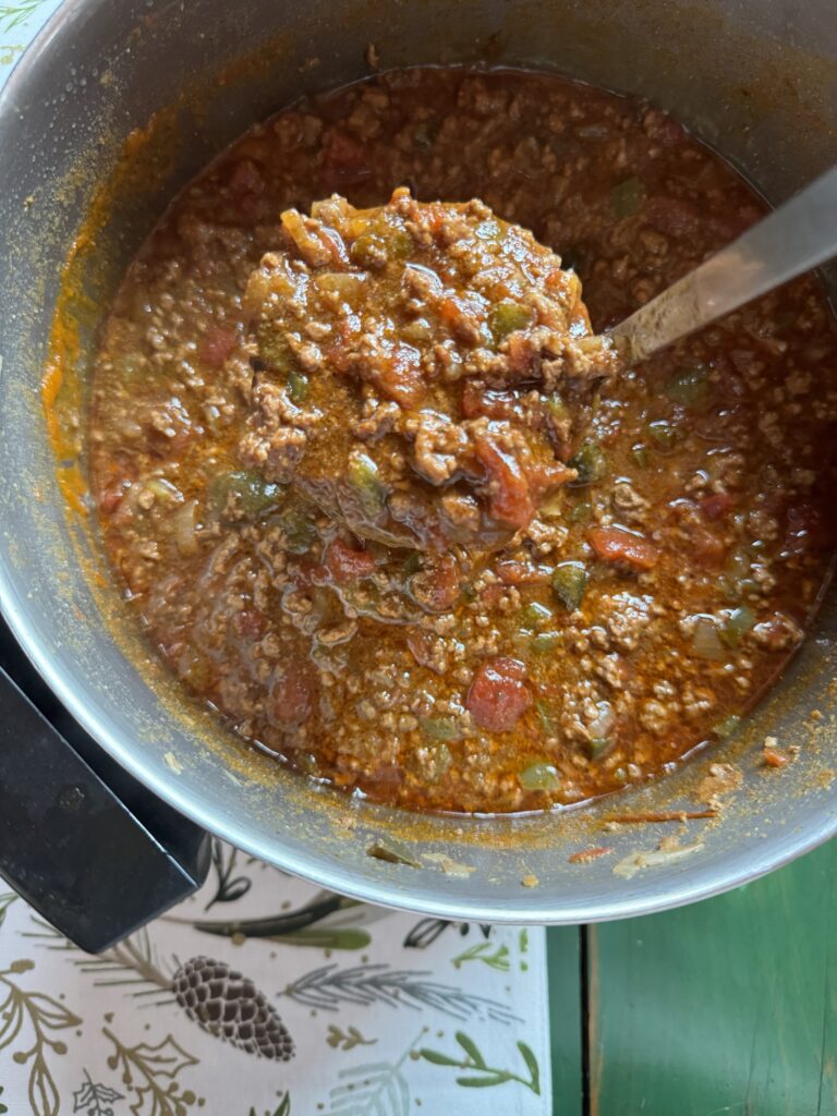 A ladle of chili above a pot of chili