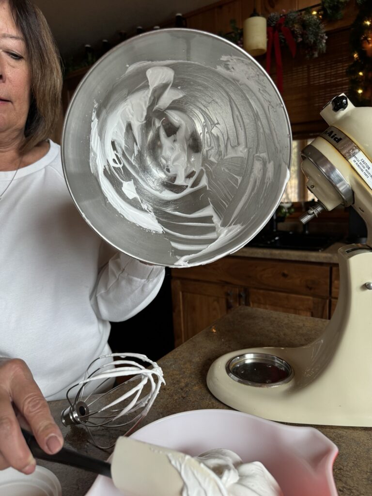 My mom showing the empty mixing bowl with traces of merengue as she uses a spatula to scrape the rest of the merengue into a bowl