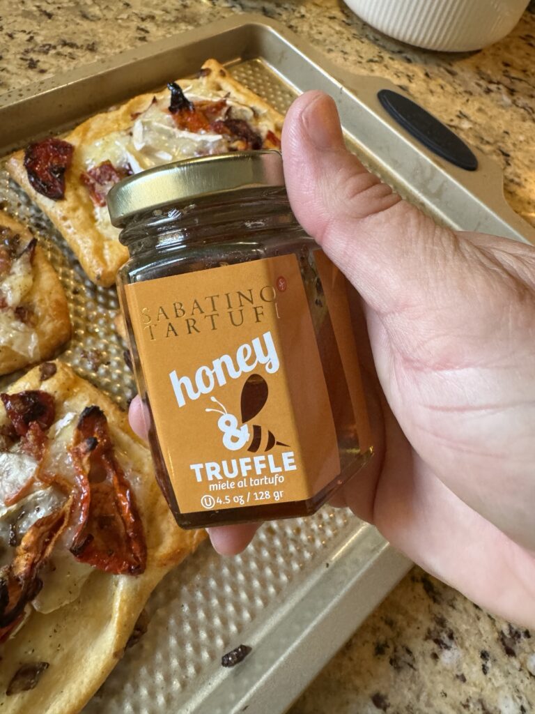 A jar of truffle honey being held above the finished tomato and brie tarts