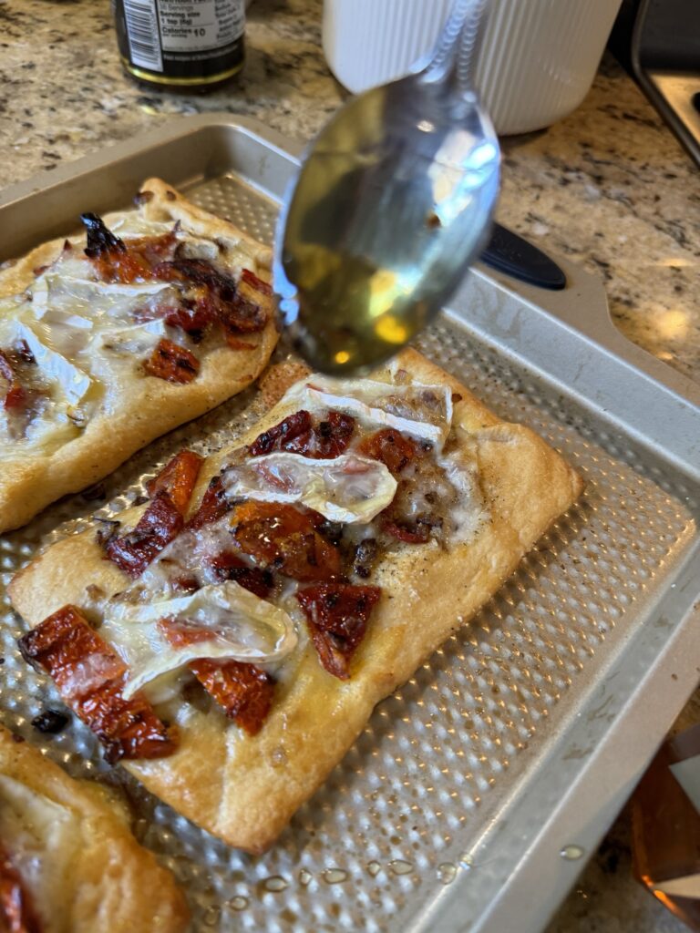 Honey being drizzled over the brie and sun dried tomato tarts with a spoon