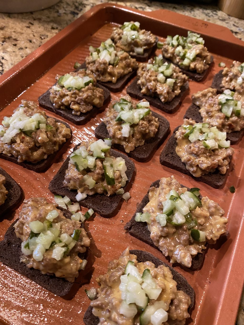 Rye toasts with meat mixture and pickle topping before baking