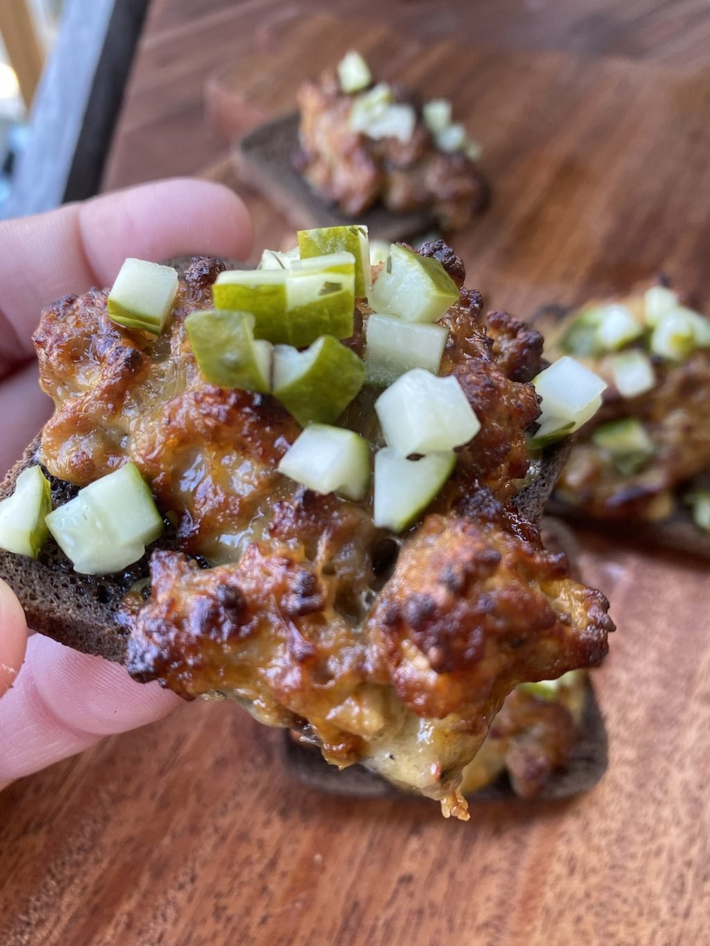 Close up of a mini rye bread slice with ground pork sausage, cheese, onions and pickles