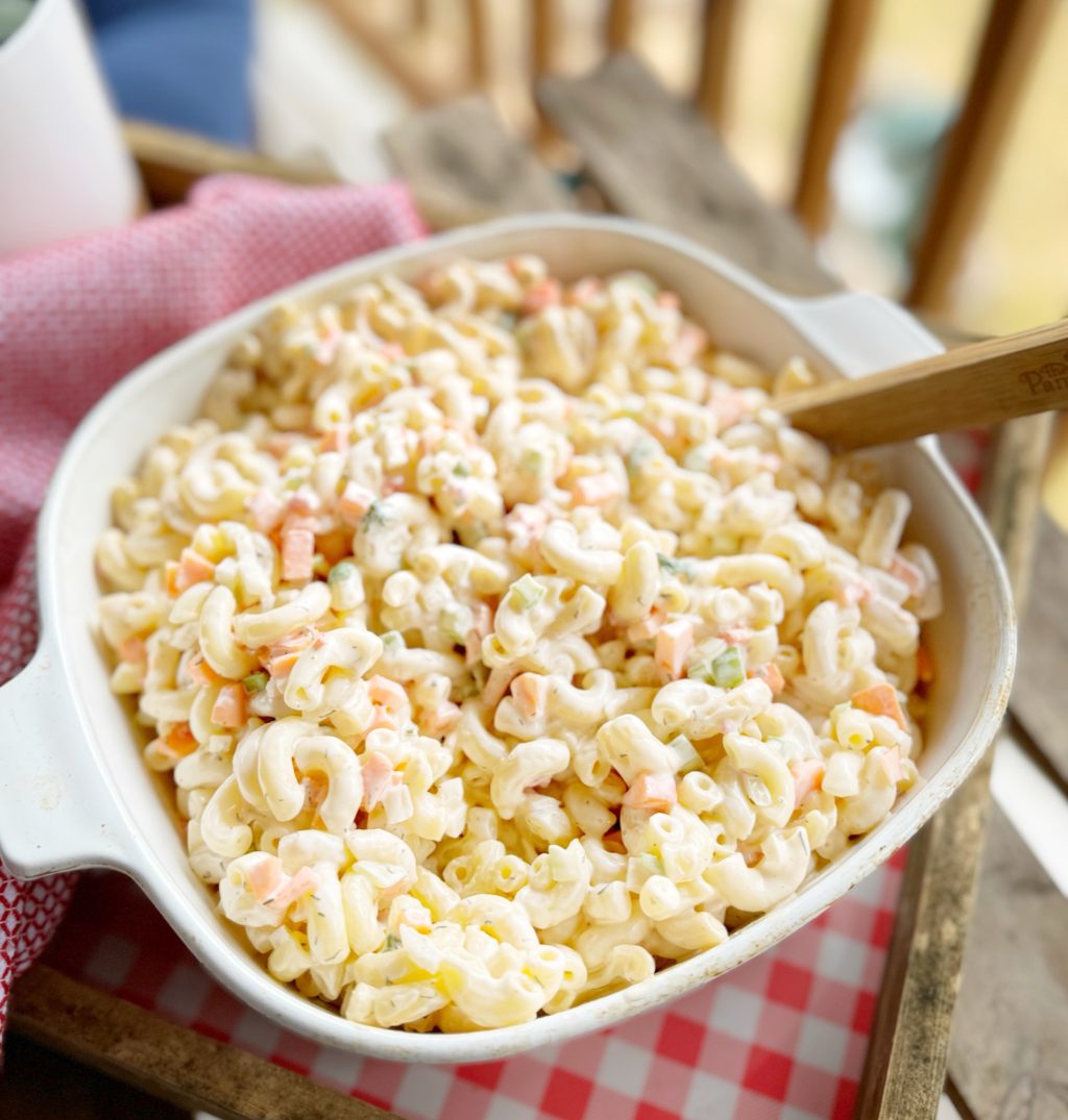 A white dish filled with macaroni salad with a wooden serving spoon