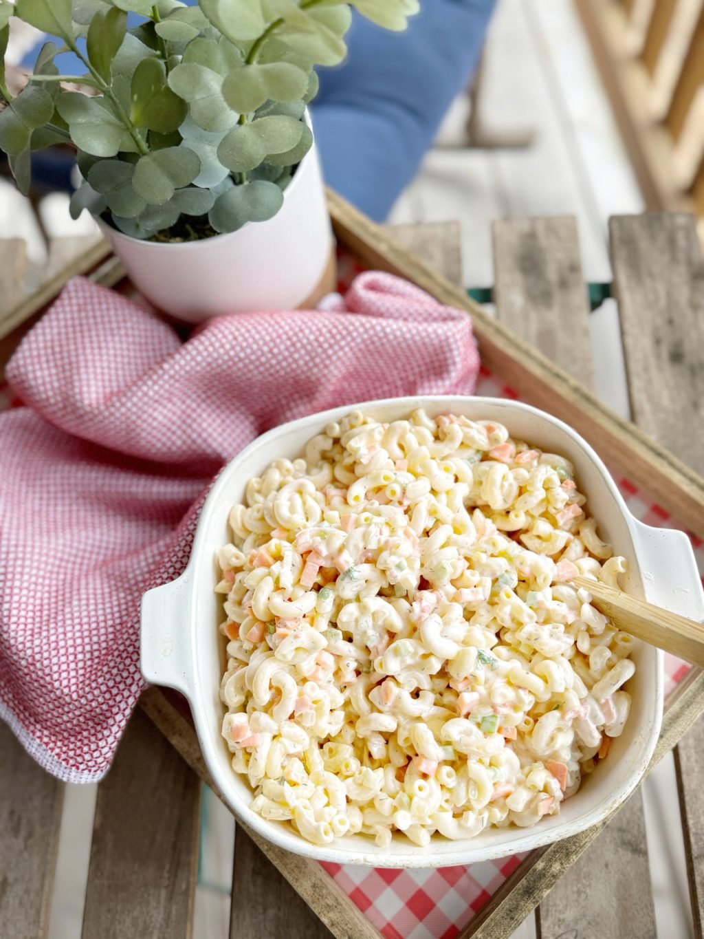 Macaroni salad in a dish with a wooden serving spoon on a white and red checkered base seen from above