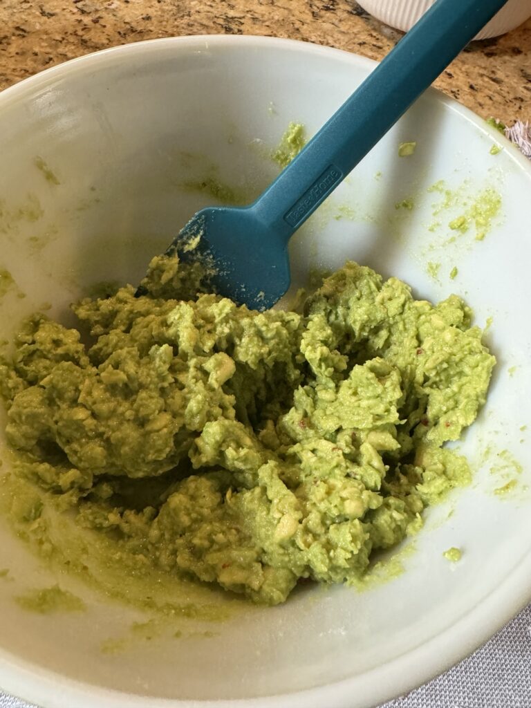 An avocado mixture in a white bowl with a blue spatula