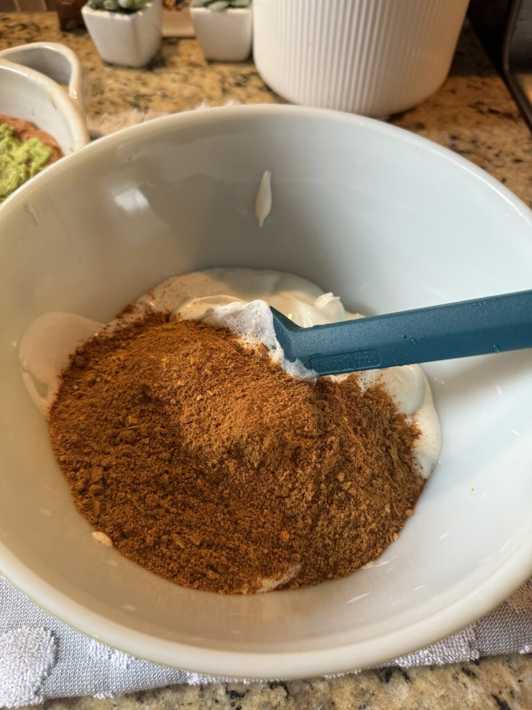 Taco seasoning on top of sour cream in a white bowl with a blue spatula