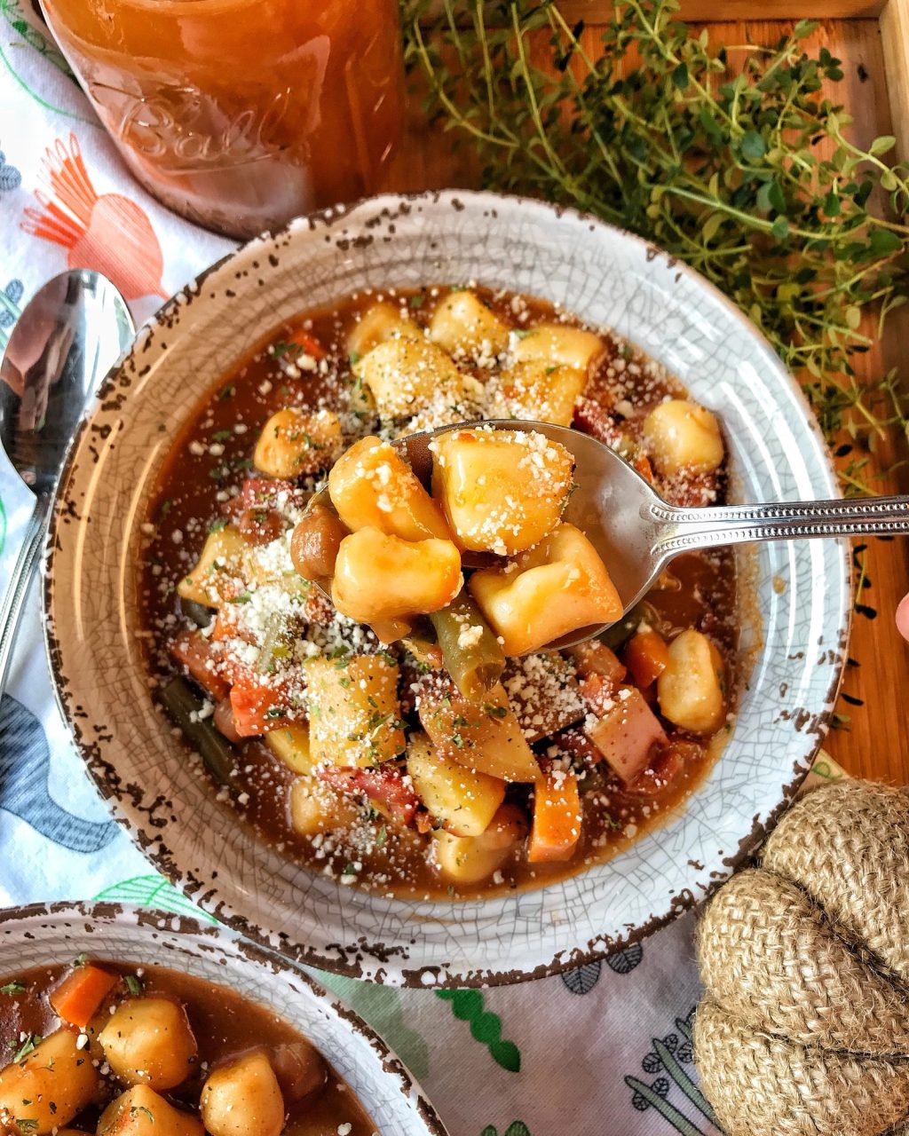 A spoon of mini potato dumplings on a spoon held over a bowl of minestrone soup