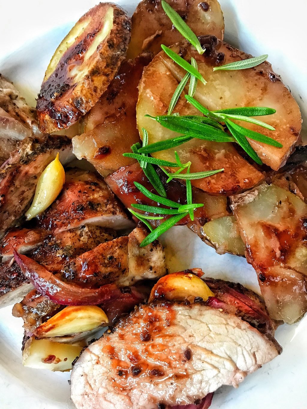 The cooked pork, sliced with the potatoes, onion, rosemary, and garlic