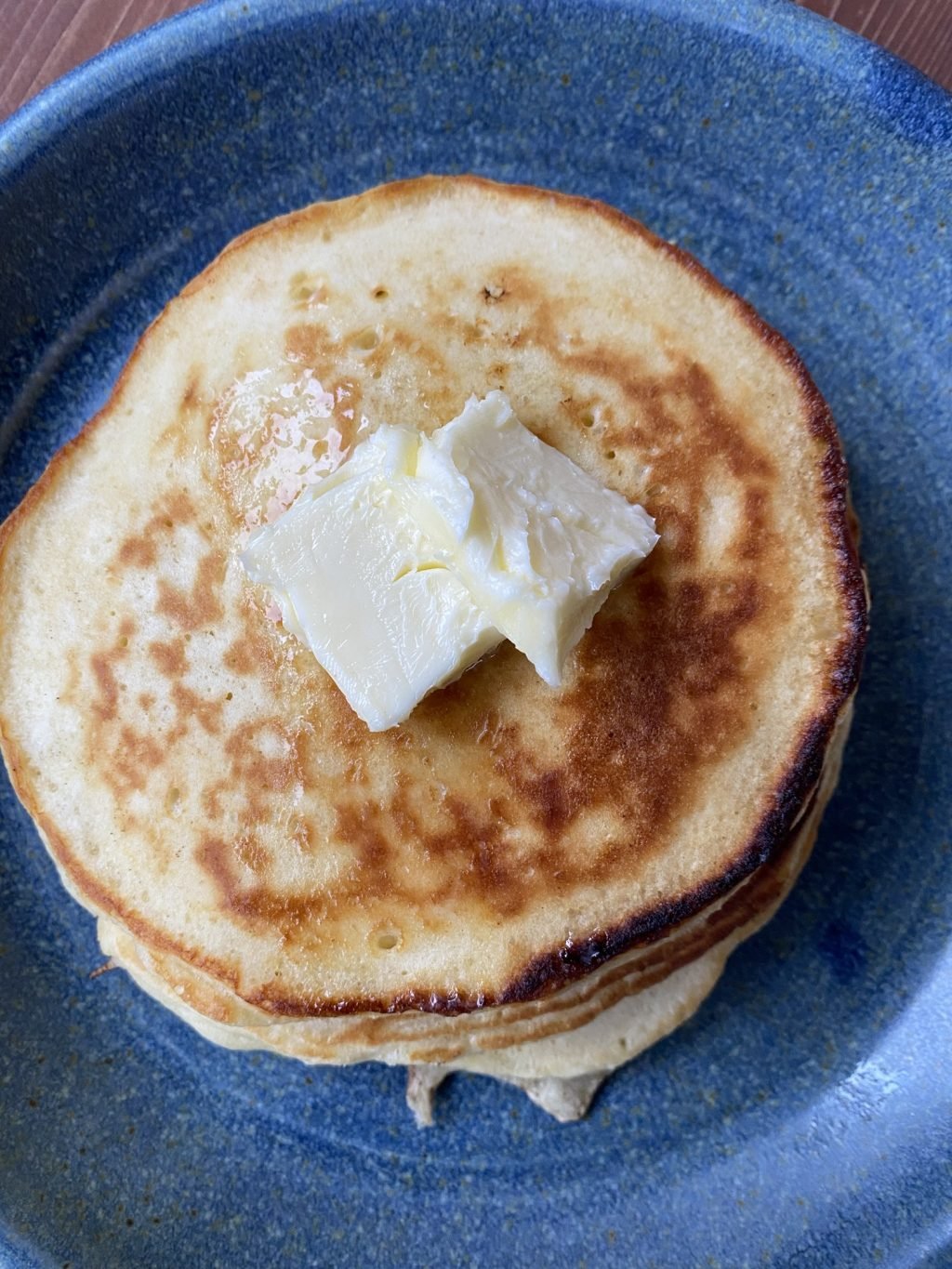 A stack of pancakes on a blue plate with butter on top