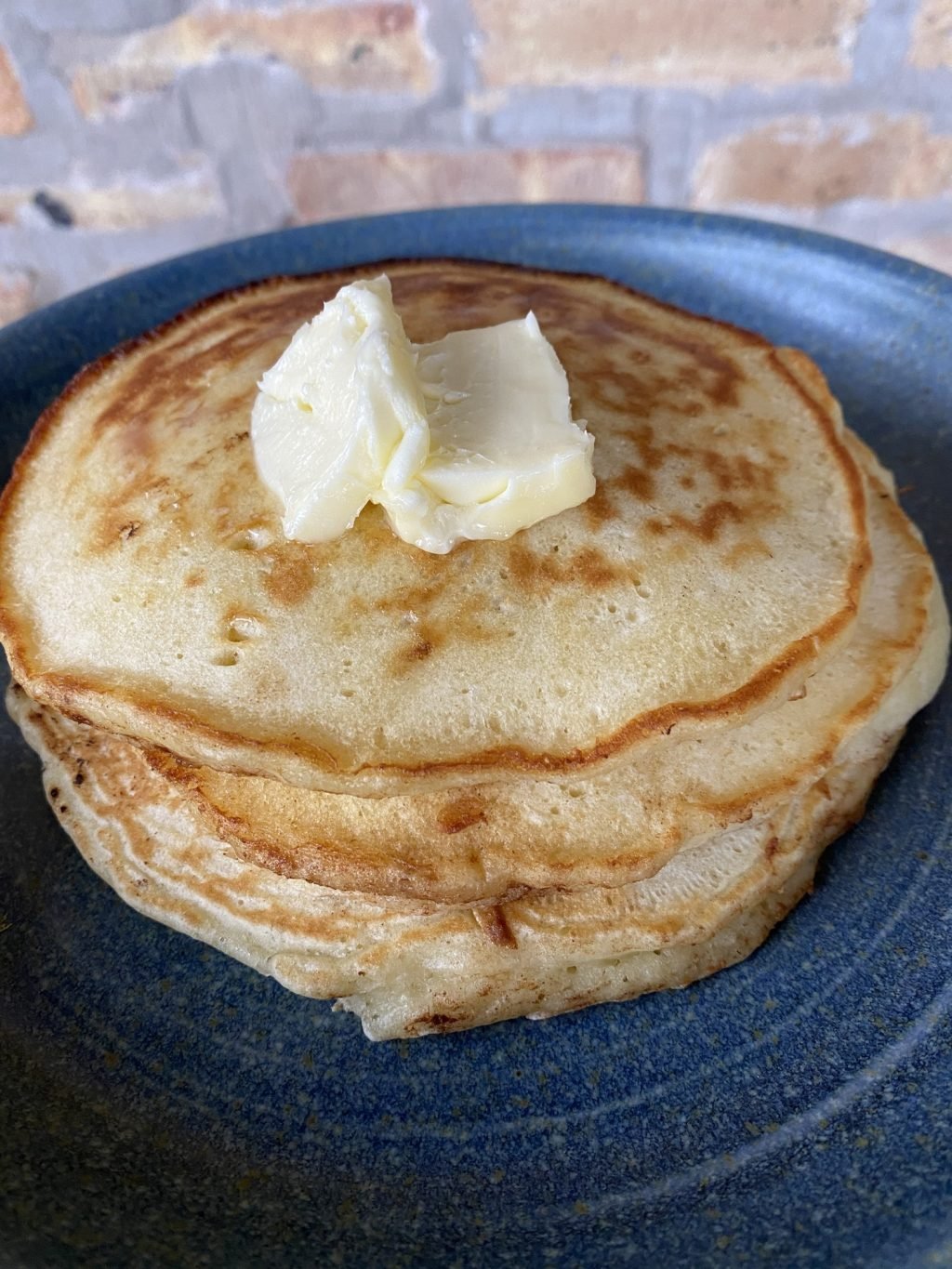 Three pancakes on a blue plate with two pats of butter on top