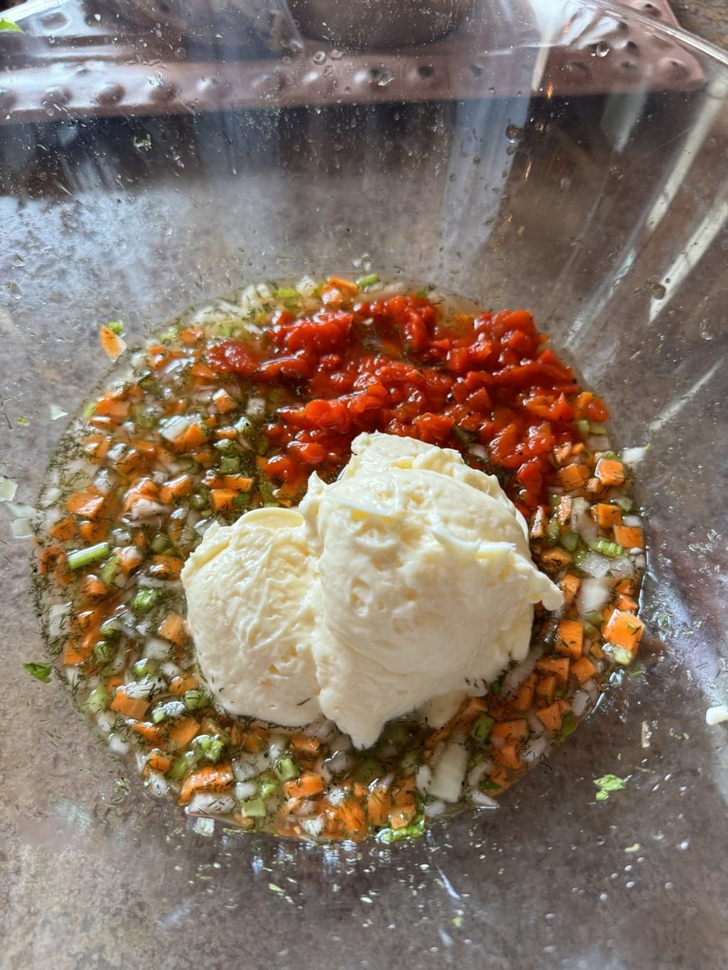 A dollop of may on top of the vegetable and vinegar mixture in a glass bowl