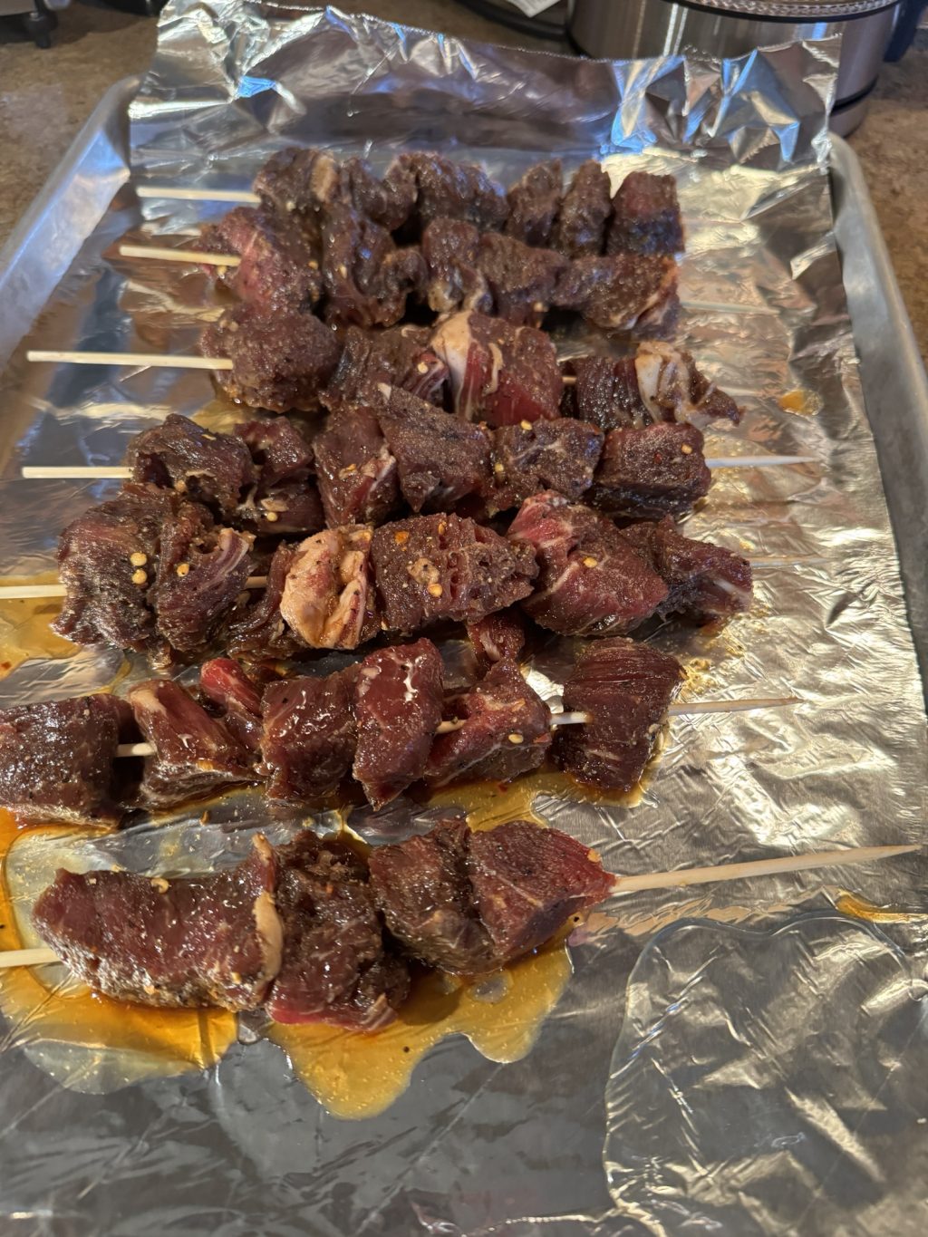 Raw, marinated beef skewers on a foil sheet