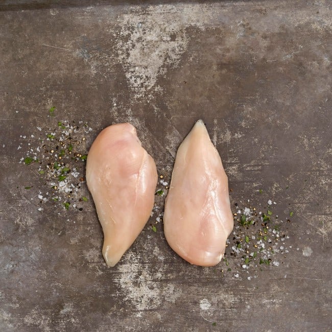 Two raw chicken breasts on a stone counter