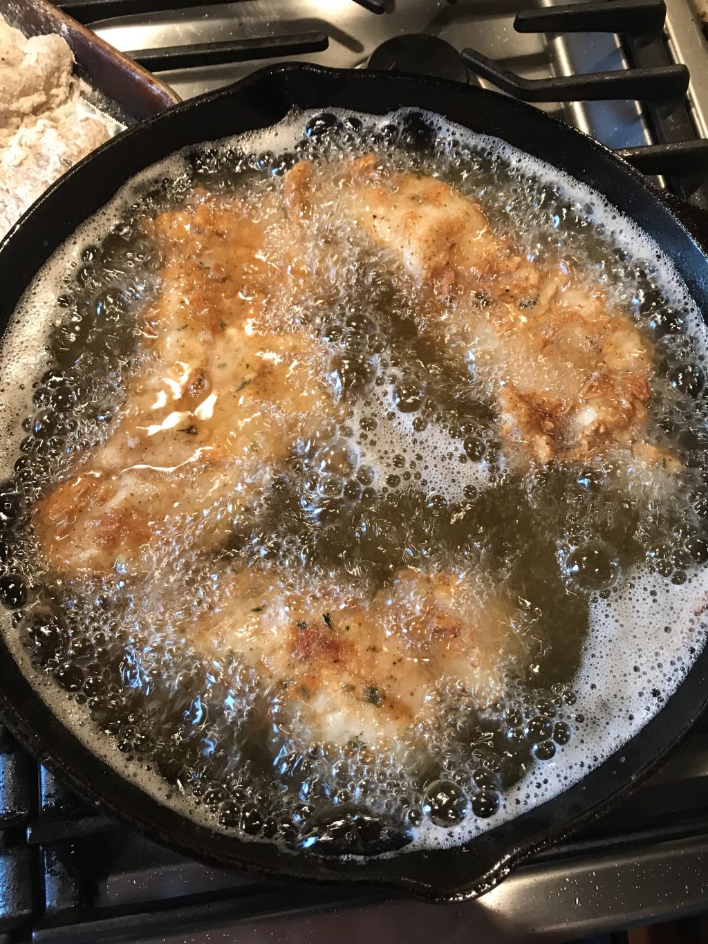 Chicken breasts frying in oil in a cast iron pan