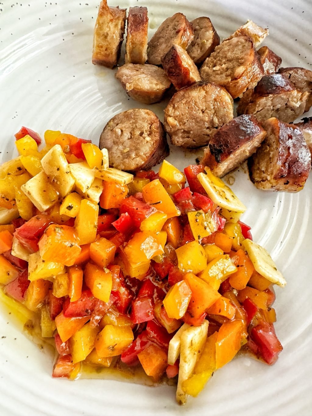 Sliced pieces of sausage on a plate next to chopped, marinated peppers with pieces of provolone cheese mixed in
