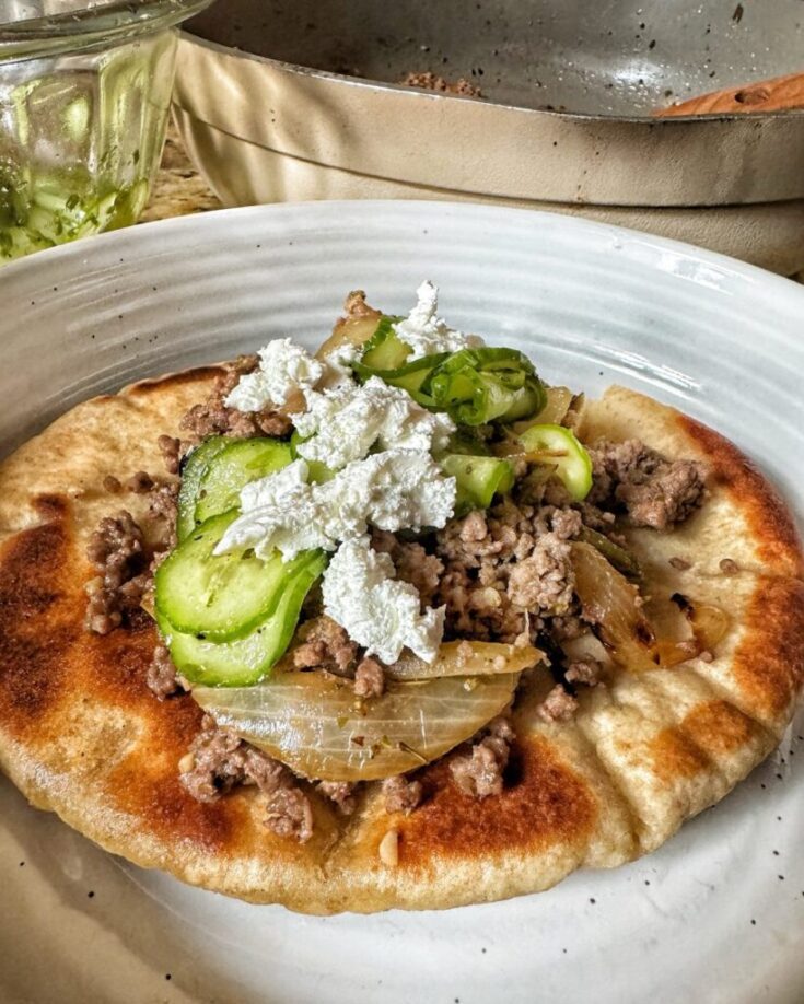 gray plate with a toasted pita bread, savory ground beef crumble, peppers and onions and a marinated cucumber salad topped with white feta cheese