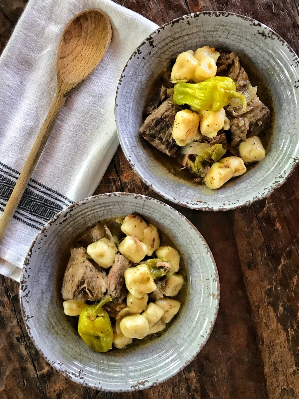 The finished Italian beef stew in two bowls next to a spoon on a kitchen towel