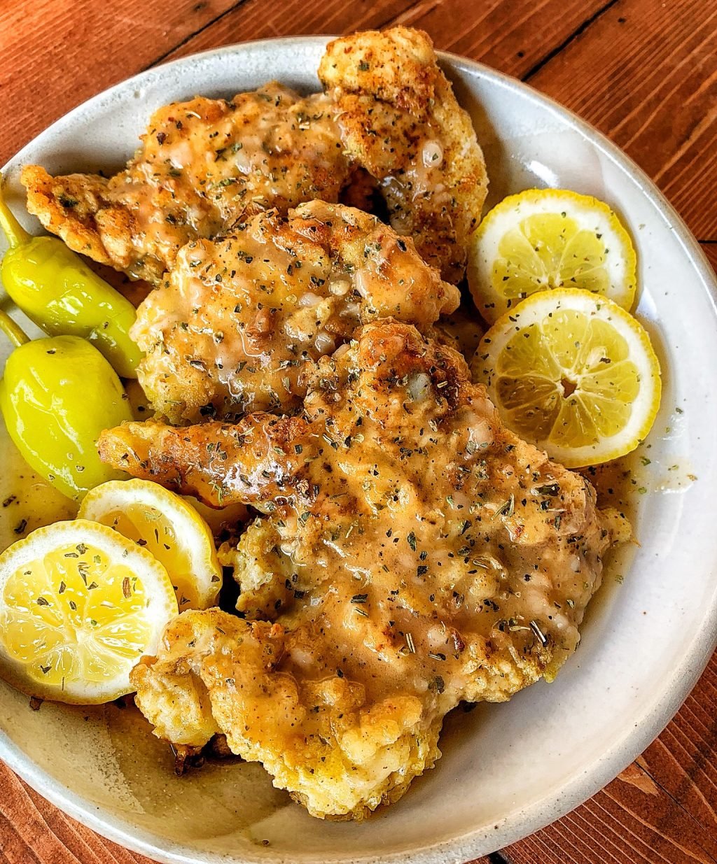 Breaded chicken cutlets with lemon slices, peperoncini peppers, and sauce on a white plate